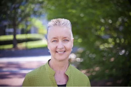 Lynne Huffer -- a human with short light hair and blue eyes in lime green jacket smiling