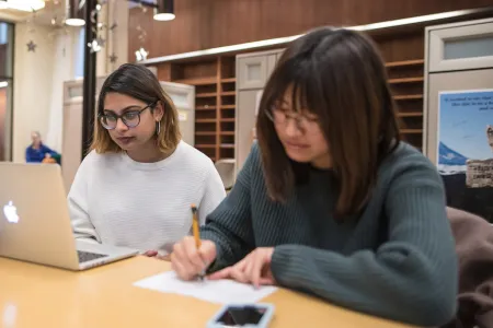 A photo of a student working on a laptop and a student writing.