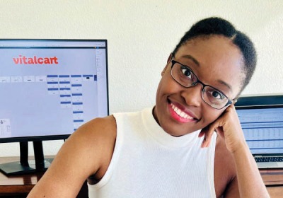 Portrait of Adaobi Kanu seated in front of a computer, the monitor displaying the Vitalcart extension