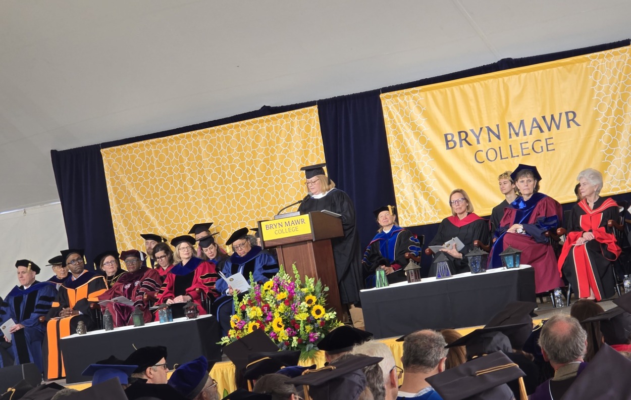 picture of Chris Boyland speaking at Wendy Cadge's Inauguration ceremony.  She is at the podium speaking, surrounded by other graduation speakers and dignitaries