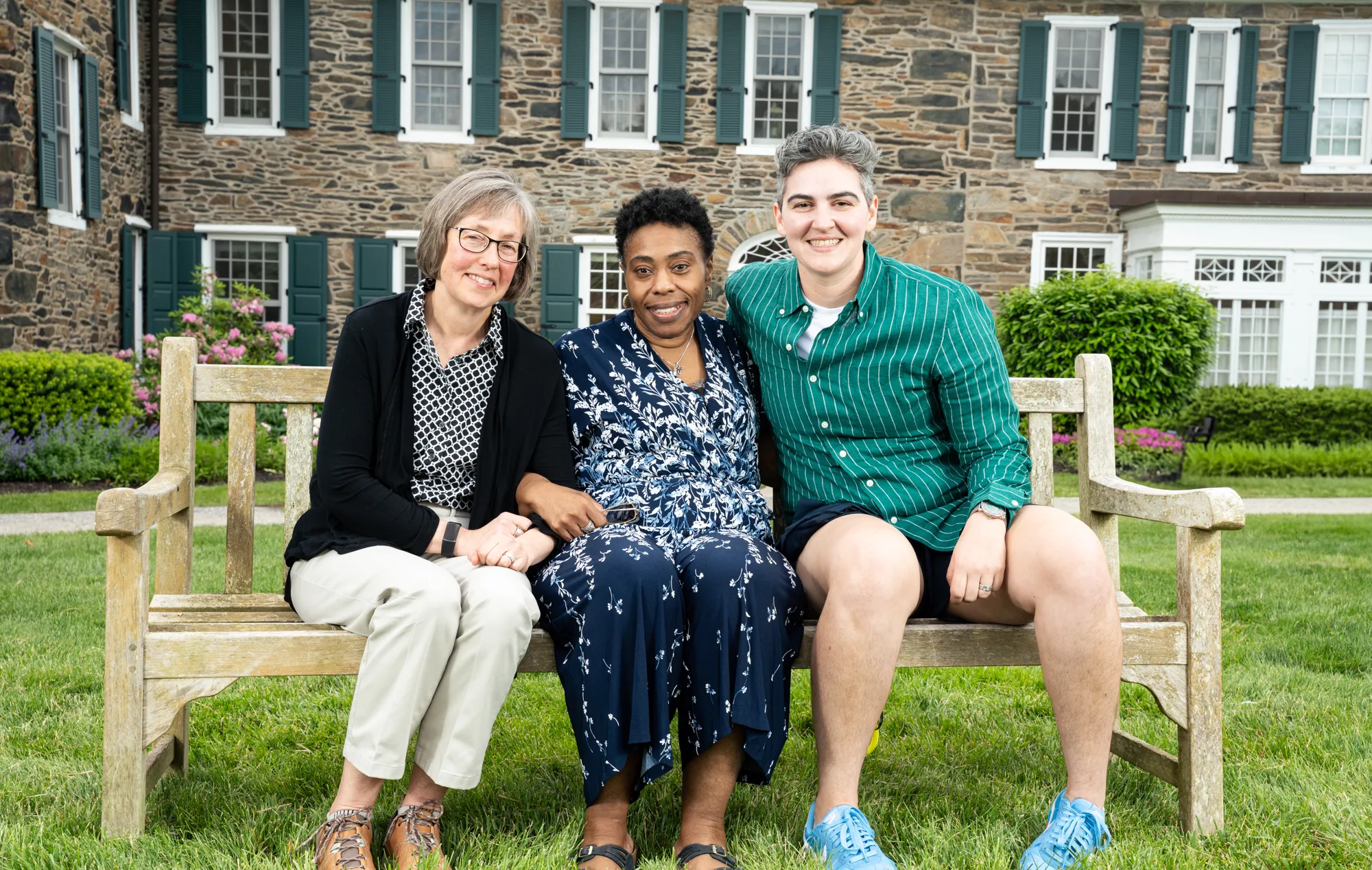 Three alums sit on a bench in front of Wyndham Alumnae House