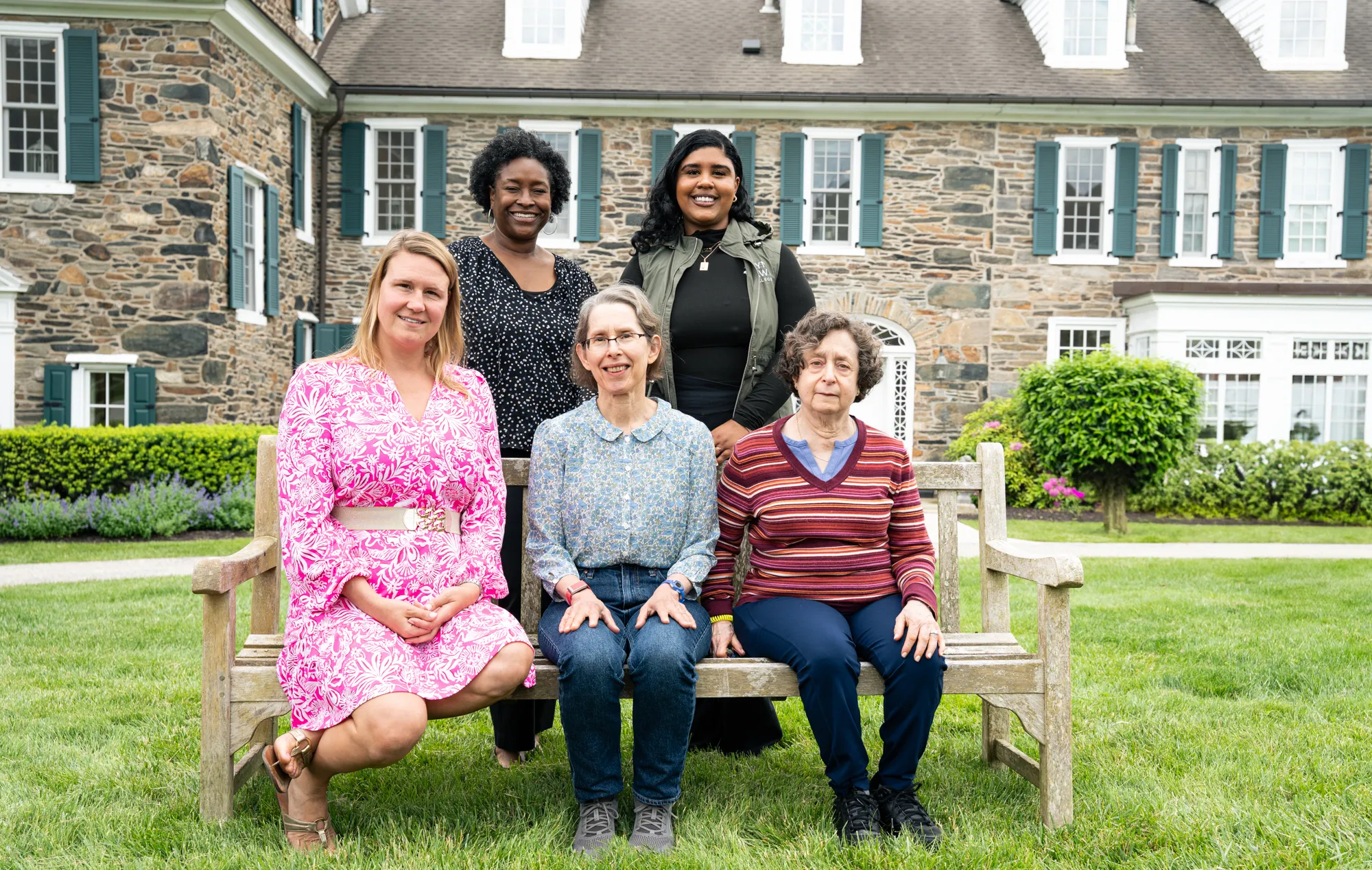A group of 5 women sit and stand in front of Wyndham Alumnae House