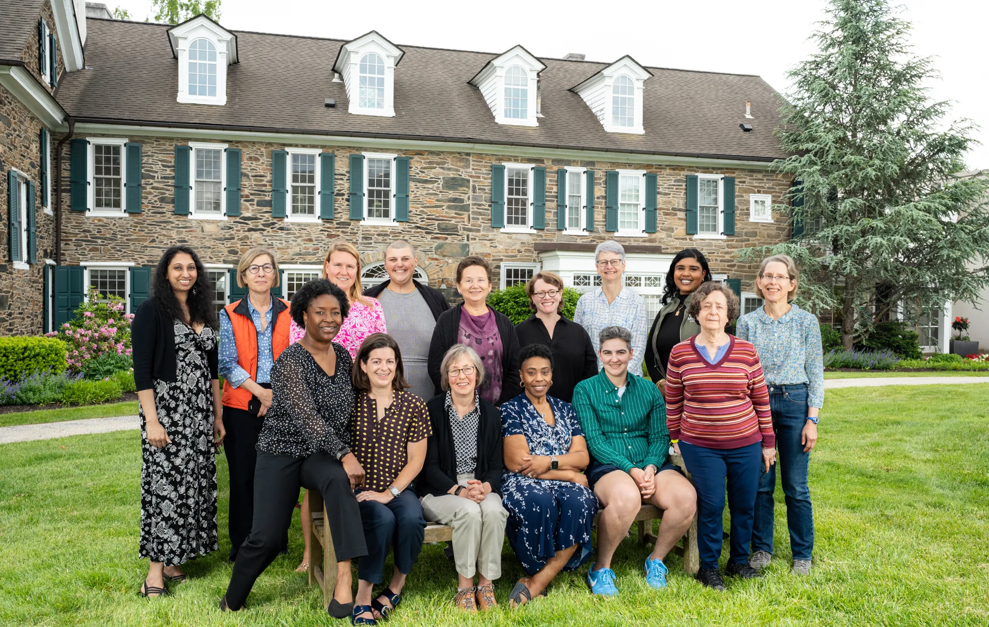 A group of multi-generational alums sit and stand in front of Wyndham Alumnae House