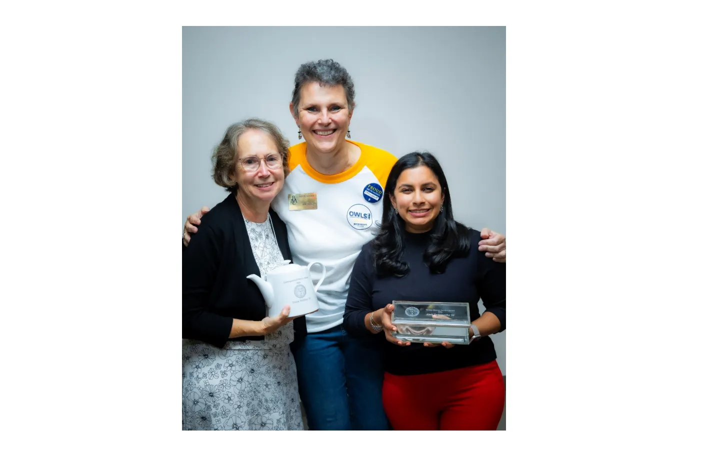 Three women smile at the camera in front of a white wall
