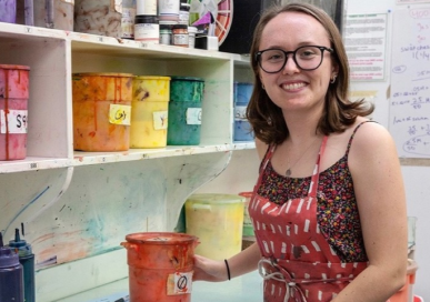 Francis Miller posing in front of paints at the Fabric Workshop and Museum in Philadelphia