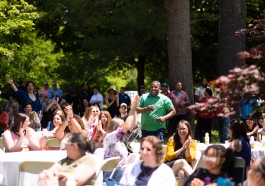 Man smiling and running through crowd of clapping people sitting at picnic tables