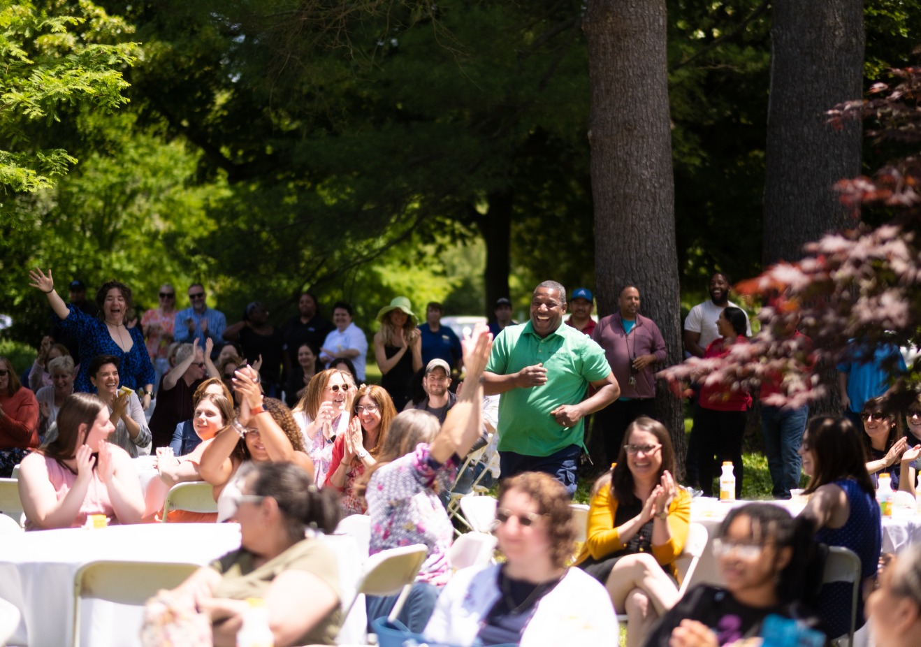 Man smiling and running through crowd of clapping people sitting at picnic tables