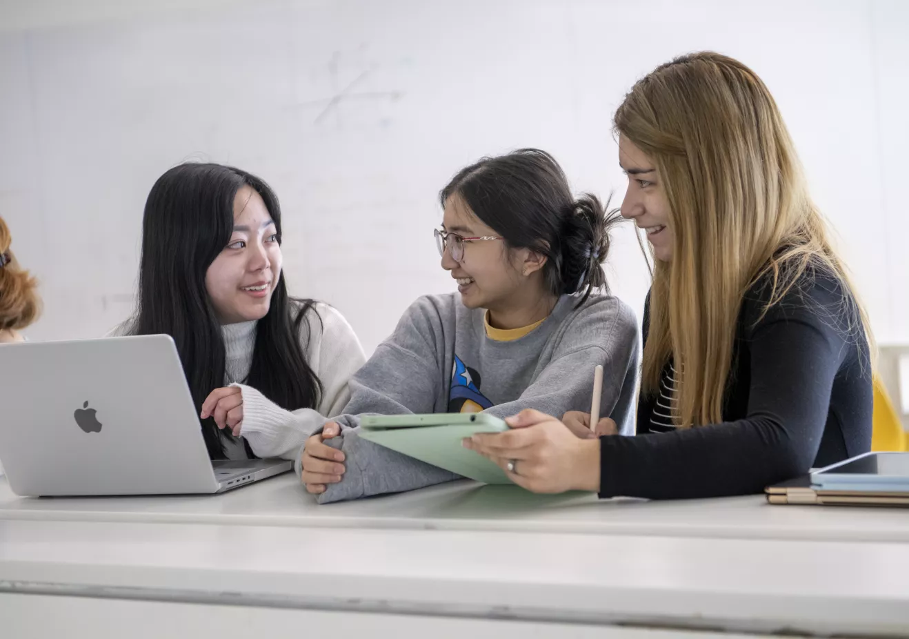 Students smiling at each other while holding a laptop and iPad 