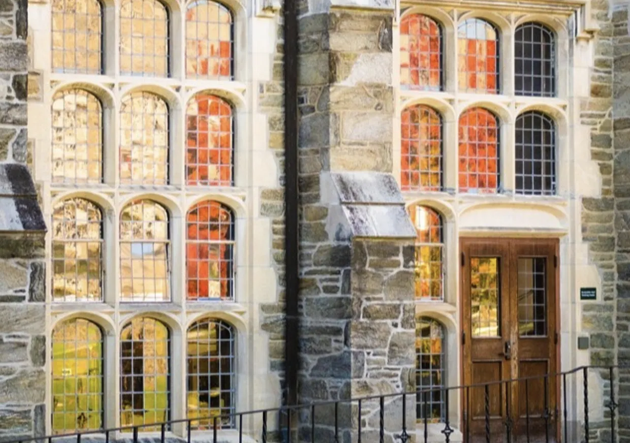 Tree with orange leaves reflected in the windows of a stone building.