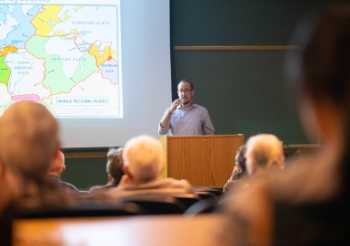 Professor next to map speaking to seated audience