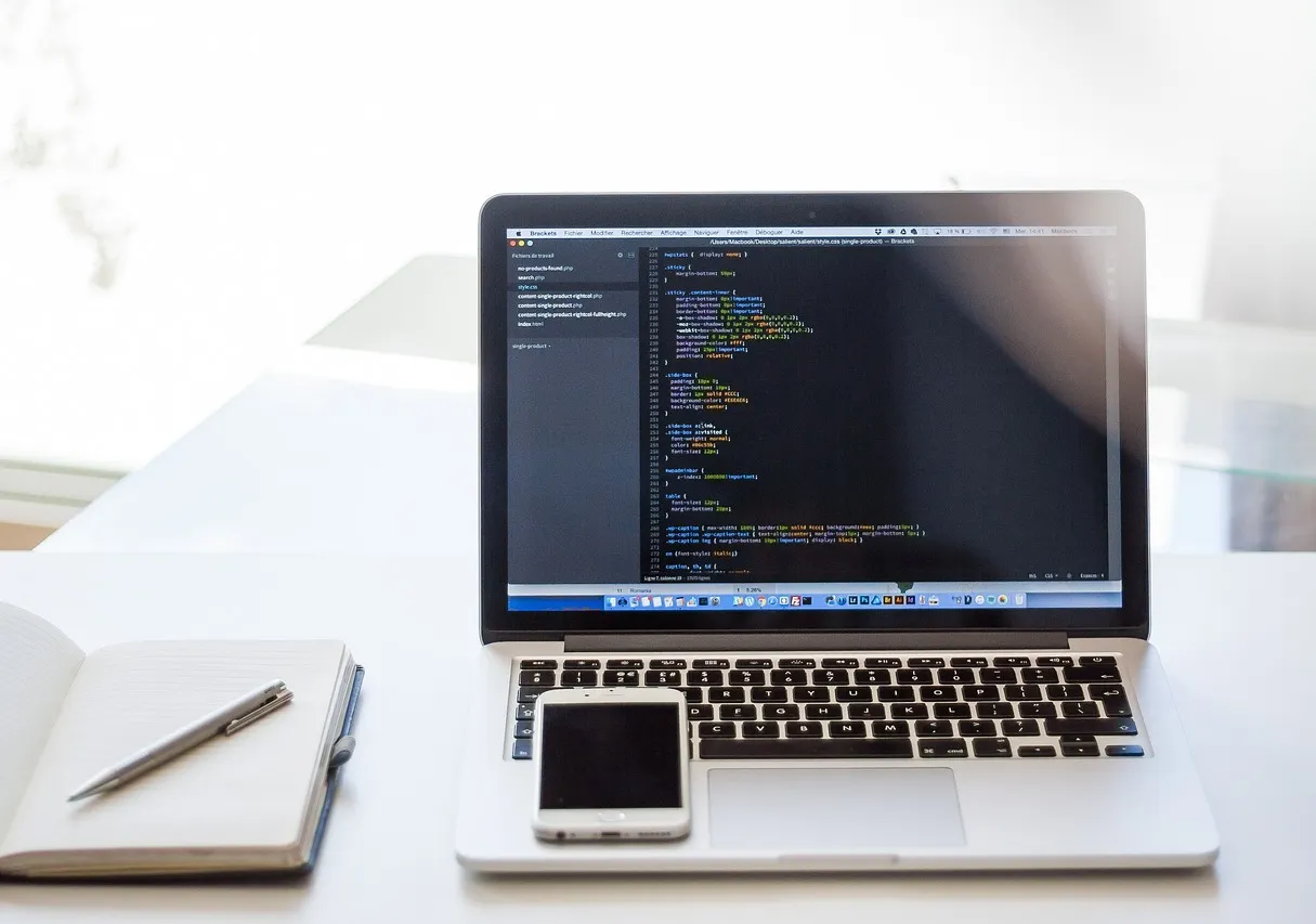 Laptop with code, notebook, and cell phone