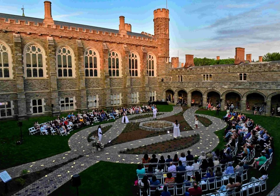 The cloisters at sunset, showcasing the Don't Forget to Remember Me monument. A crowd is seated at each side of the monument.