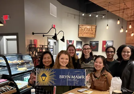 A group of women smile at the camera while standing in a cafe