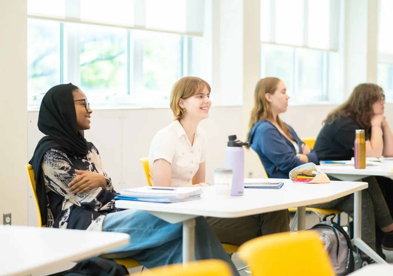 4 students sit at white desks in a brightly lit classroom