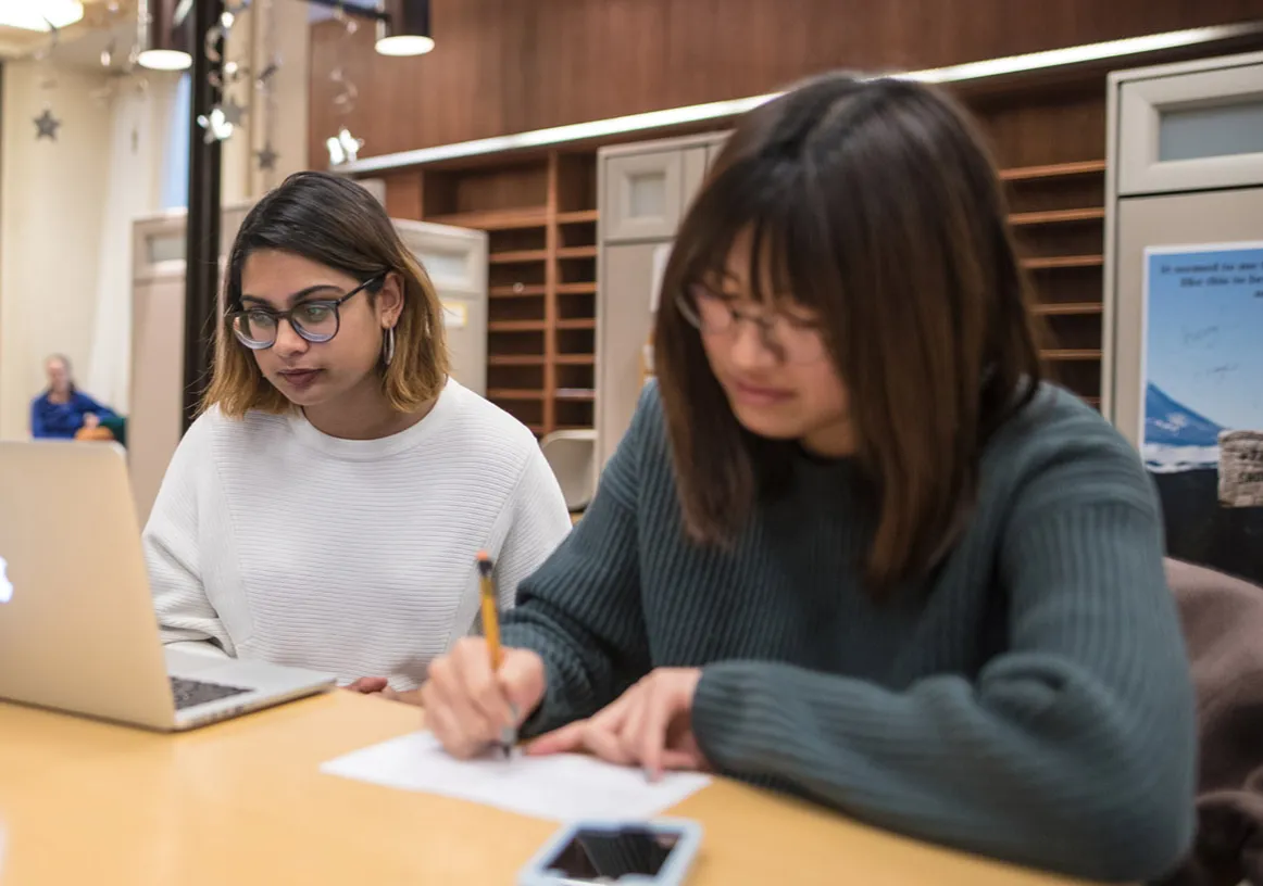 A photo of a student working on a laptop and a student writing.