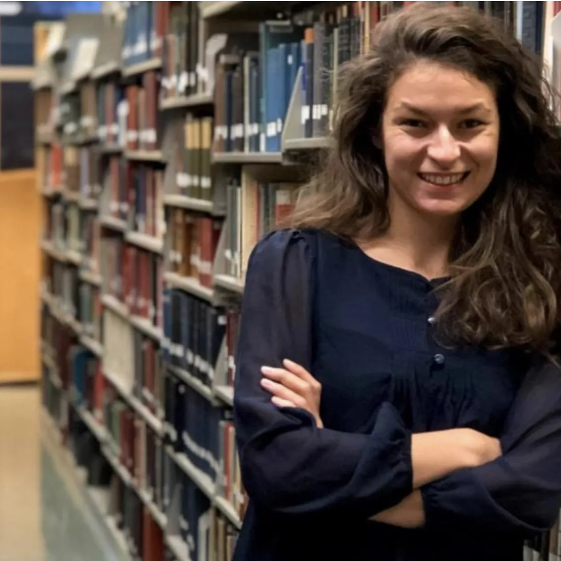 woman with long brown hair standing next to a row of bookcases