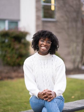 Joi Dallas sitting and smiling in front of the New Dorm. 