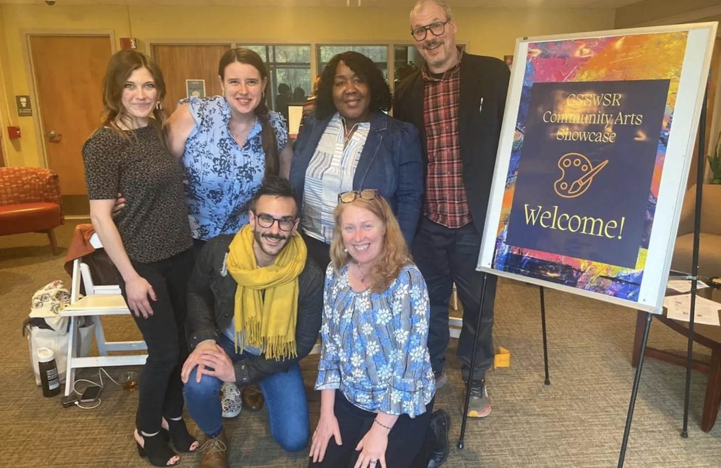 Six members of the Graduate School of Social Work and Social Research posing in a group photo in front of a "GSSWSR Community Arts Showcase Welcome!" sign