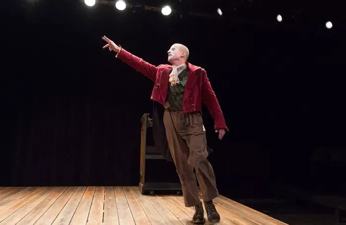 A single actor on a stage in a red jacket