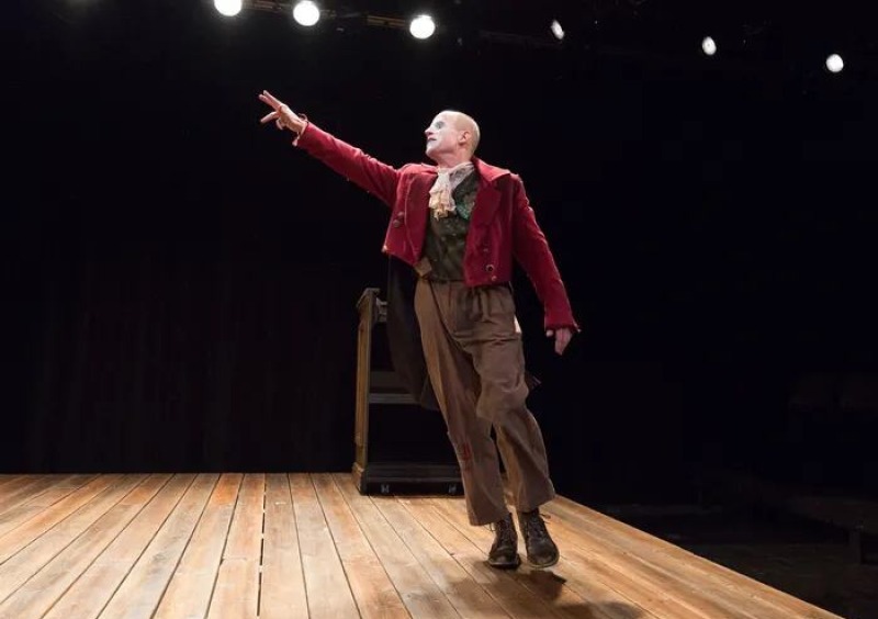 A single actor on a stage in a red jacket