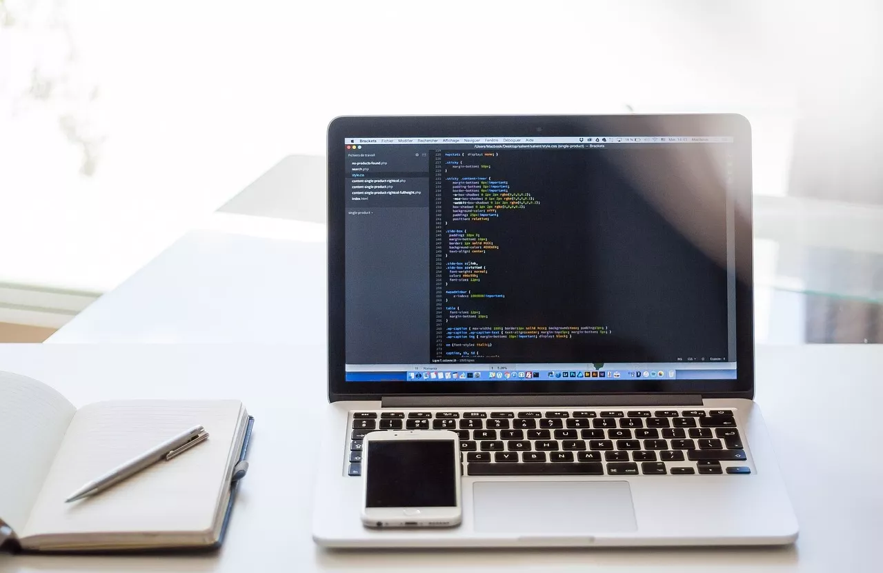 Laptop with code, notebook, and cell phone