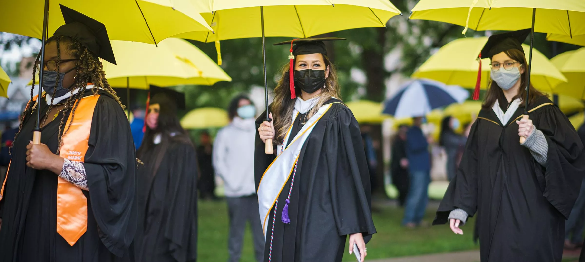 Students walk to graduation with yellow umbrellas