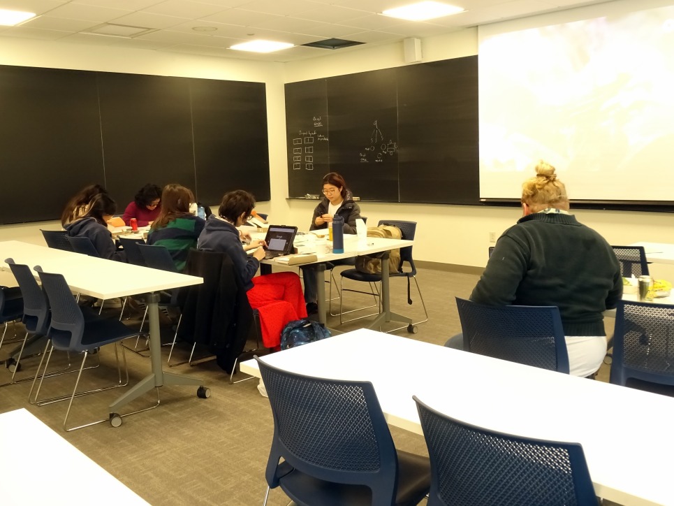 Sean Kennan '20, in the foreground, watches students, in the background and around a table, work on their devices during the physical computing intensive