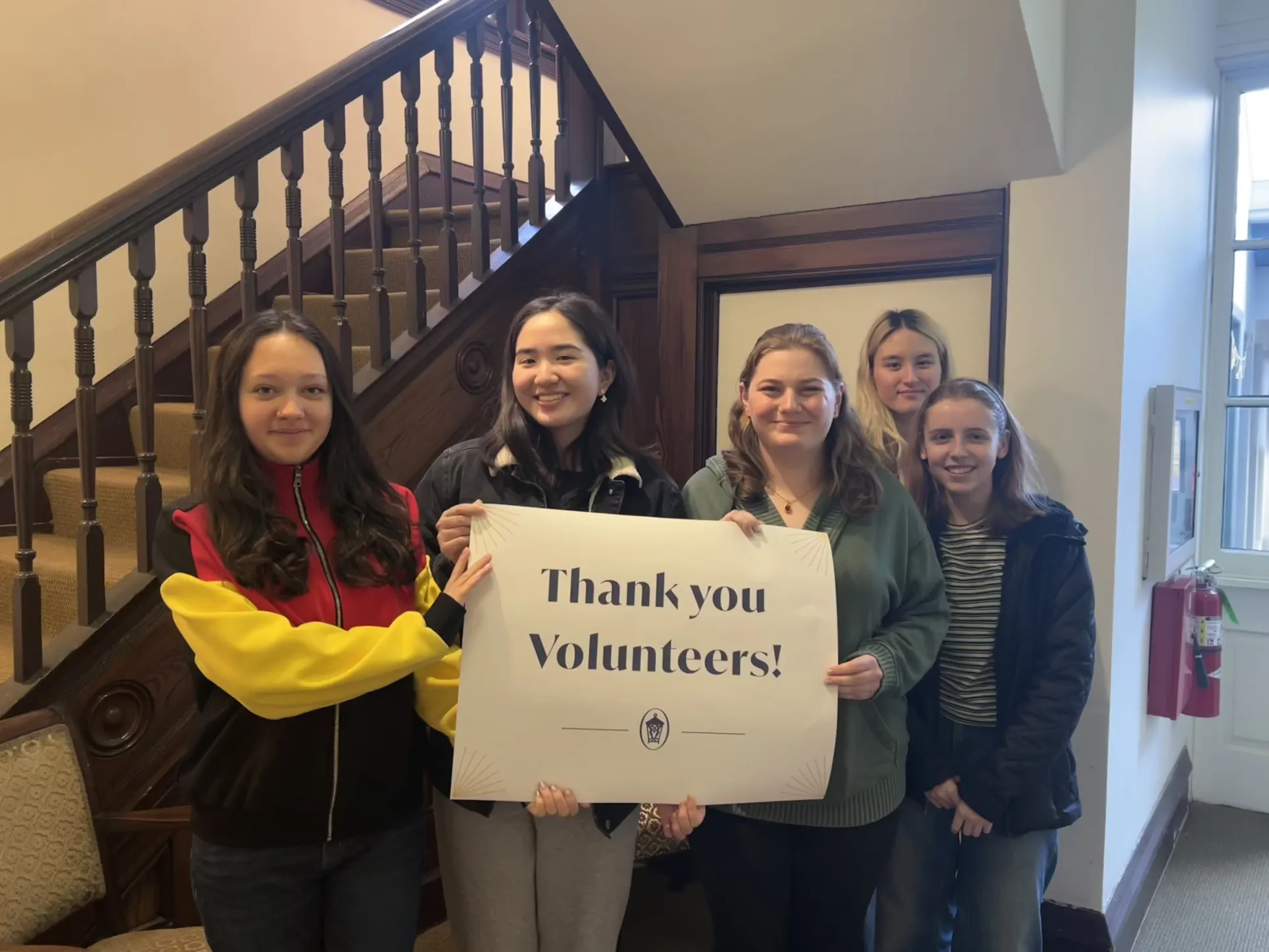 A group of students stands in front of a stairwell holding a sign that says "Thank you volunteers!"