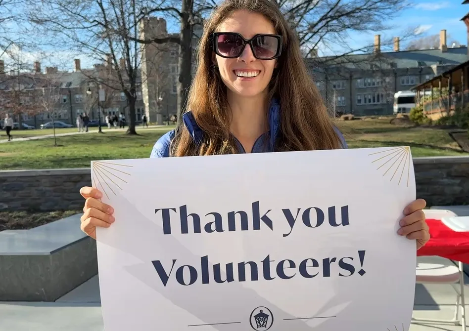 A student stands outside holding a sign that says "Thank you Volunteers!"