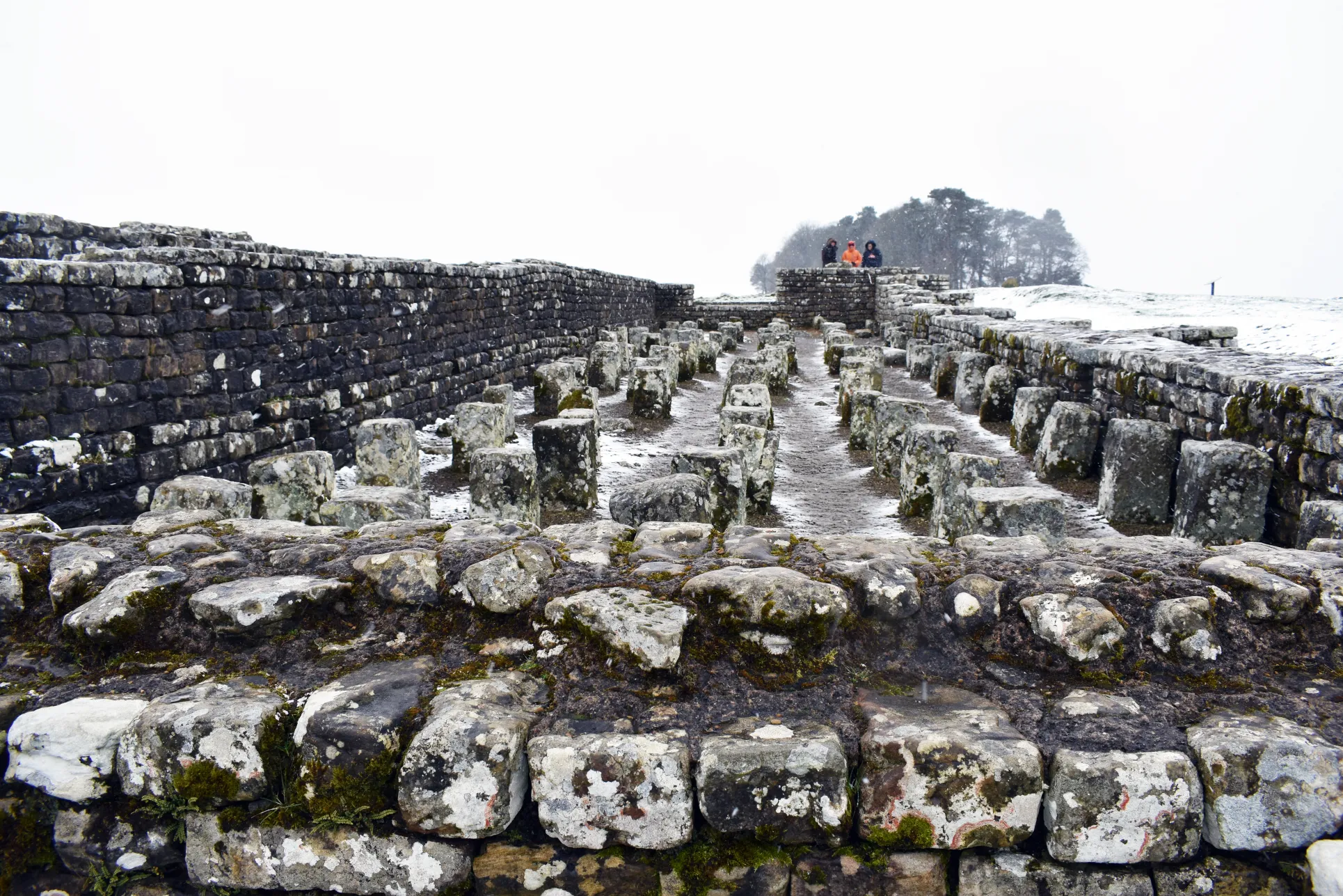 Hadrian's wall in the snow with students looking on in the distance