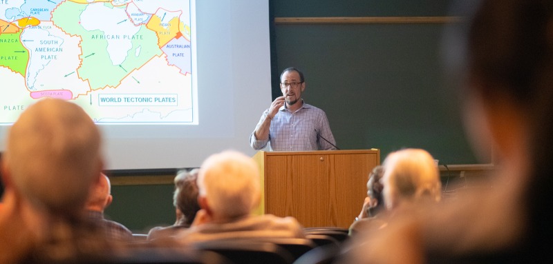 Professor next to map speaking to seated audience