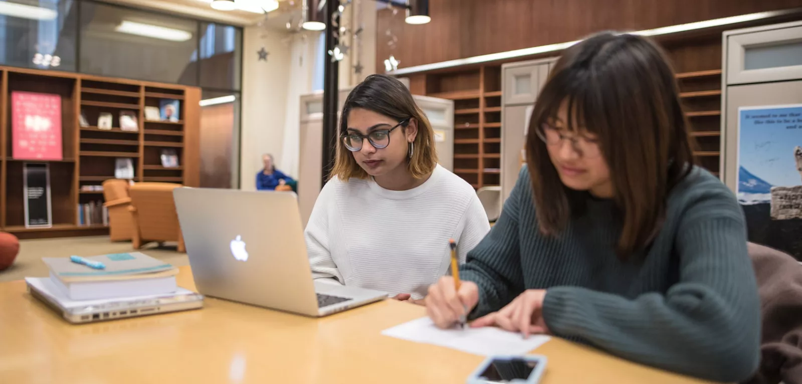 A photo of a student working on a laptop and a student writing.
