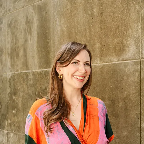 Emily Alesandrini in orange and pink shirt in front of concrete wall