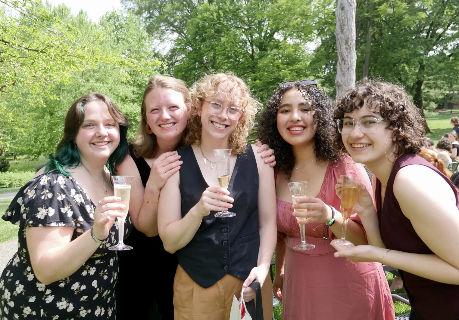 Five students crowd together and smile at the camera while toasting champagne flutes