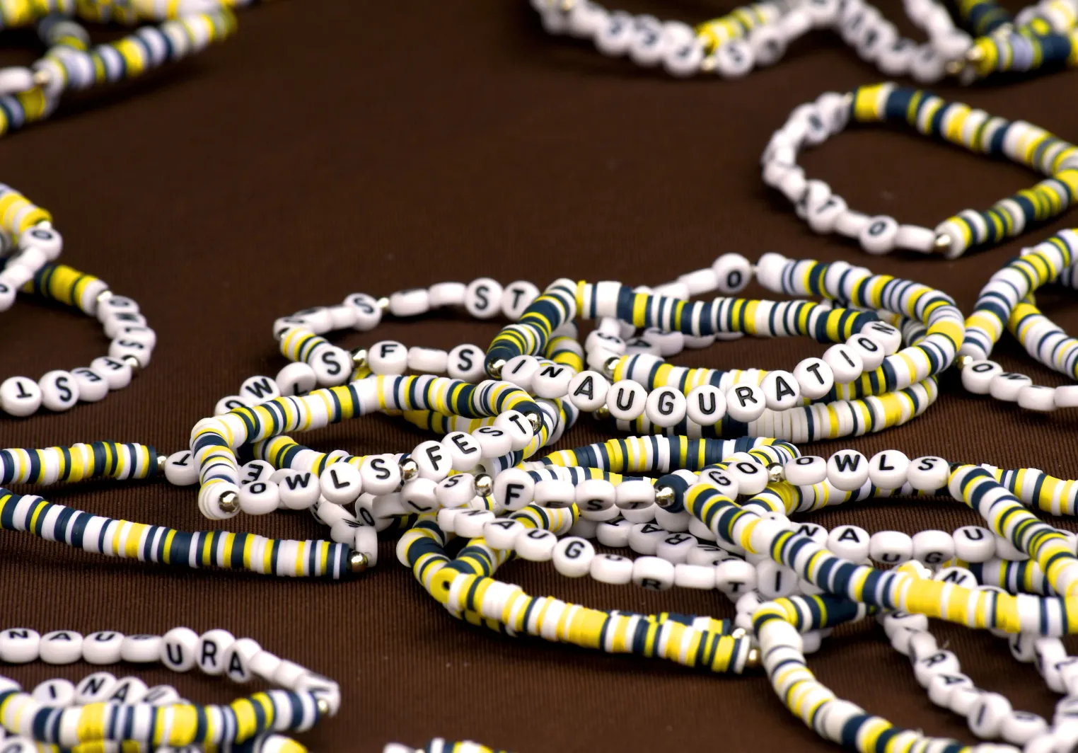 A pile of white, yellow, and navy friendship bracelets are on a table. They say Go Owls, Inauguration, and Owls Fest.
