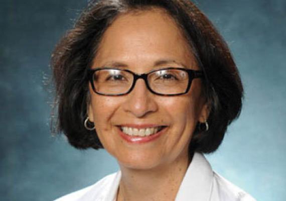 Portrait of Ana Maria López in a lab coat in front of a blue background