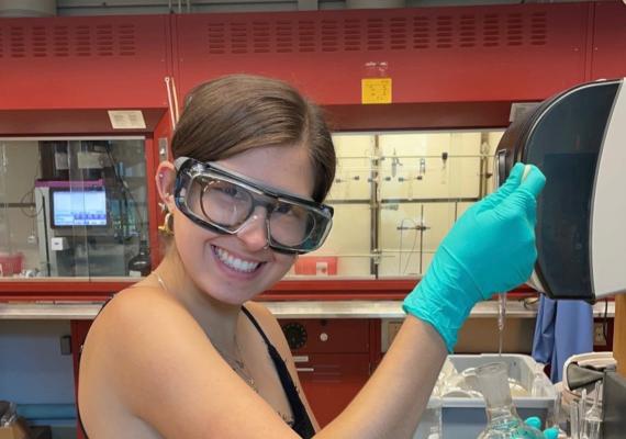 Yael Eiben smiling in the lab and filling a beaker