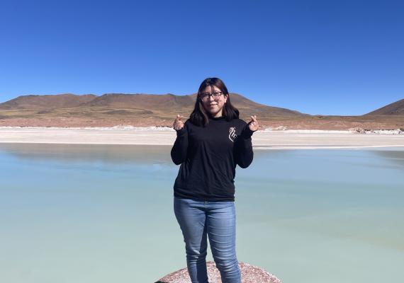 Michelle Lamadrid Benavides standing in front of a lake making finger hearts. 