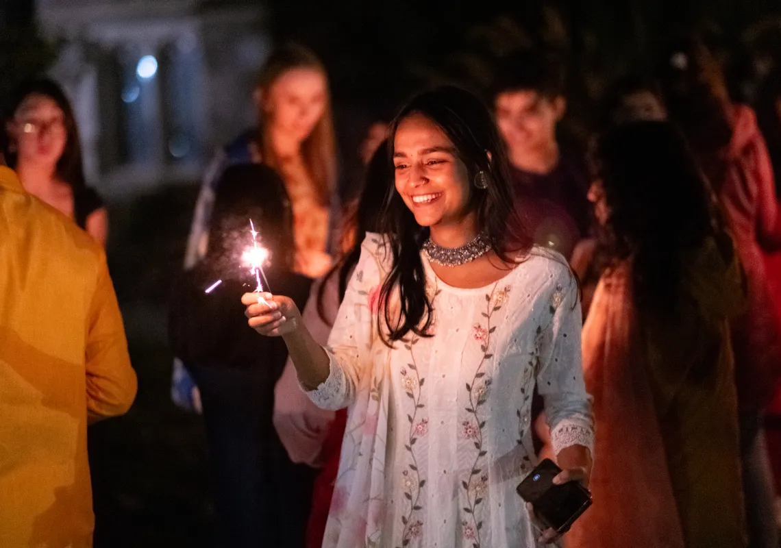 Group of smiling students at nighttime holding a sparkler