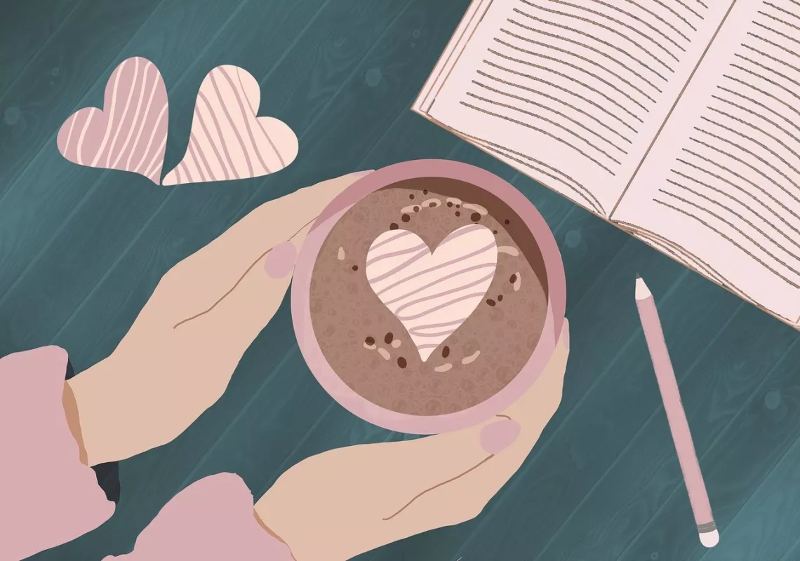 Hands holding a cup of cocoa and book