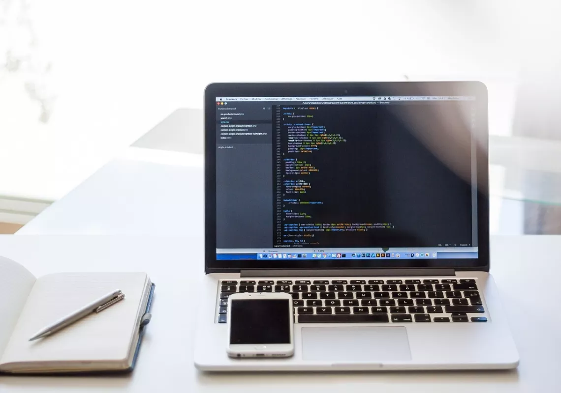 Laptop with code, notebook, and cell phone