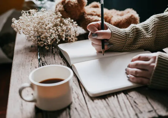 image shows a person working on a journal with a warm cup of tea