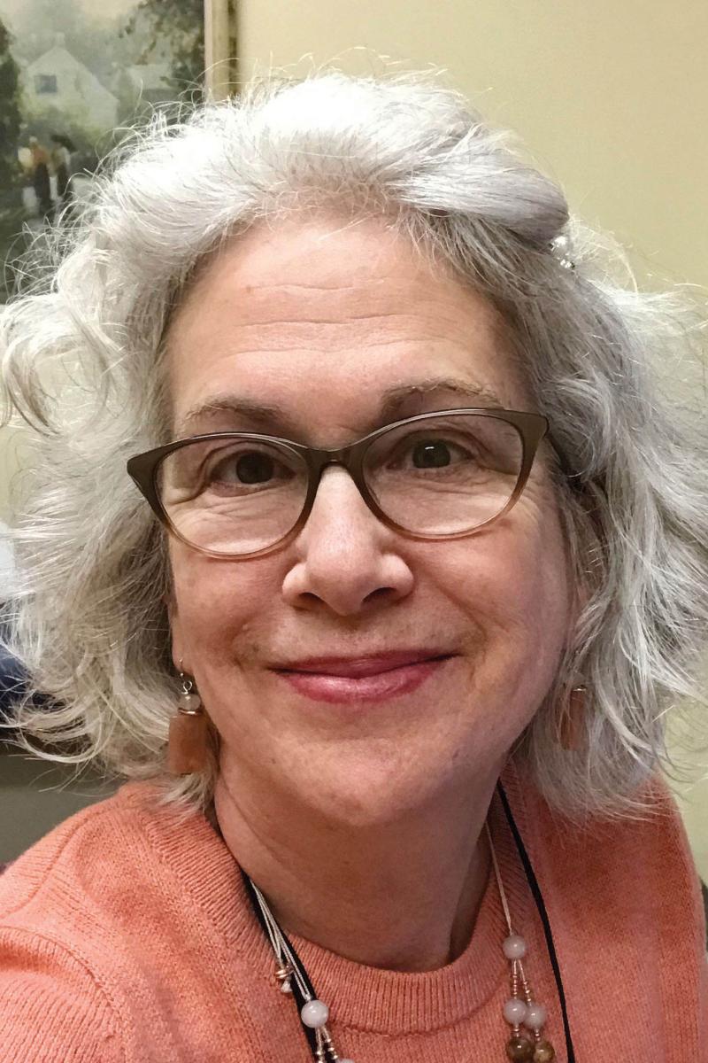 Close up portrait of Ann Smith wearing an orange tee shirt and glasses