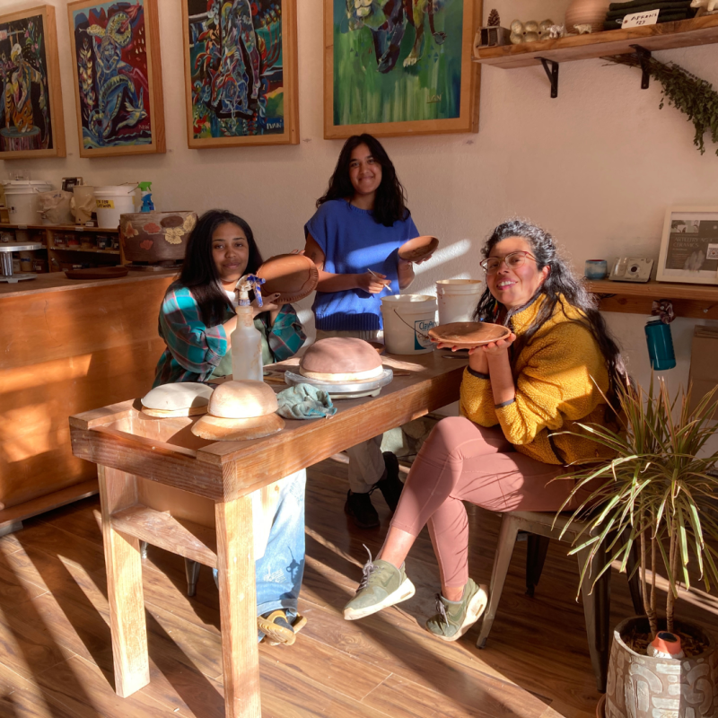 Three people in a pottery studio carving plates