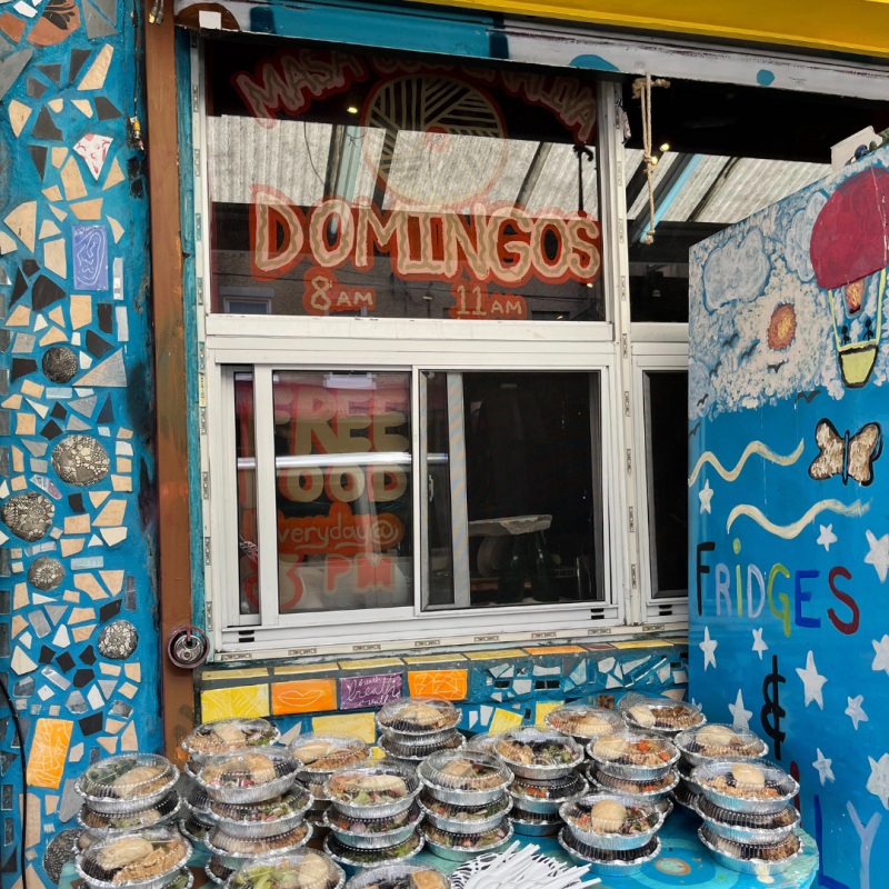 Restaurant pick-up window painted with a mural and a stack of take-out food containers. 