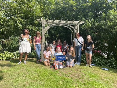 A group of students standing under a pergola and holding a BMC pennant during a Send-Off Party