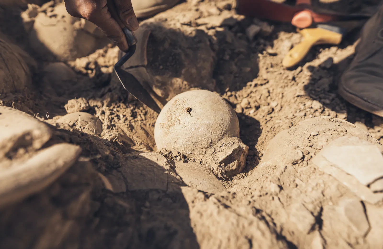A PhD archaeology student brushing of an artifact in the ground.
