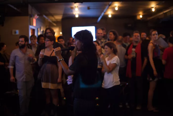 A person in profile is speaking into a microphone in a crowded room.