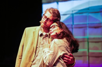 Two actors embrace in front of colorful screen